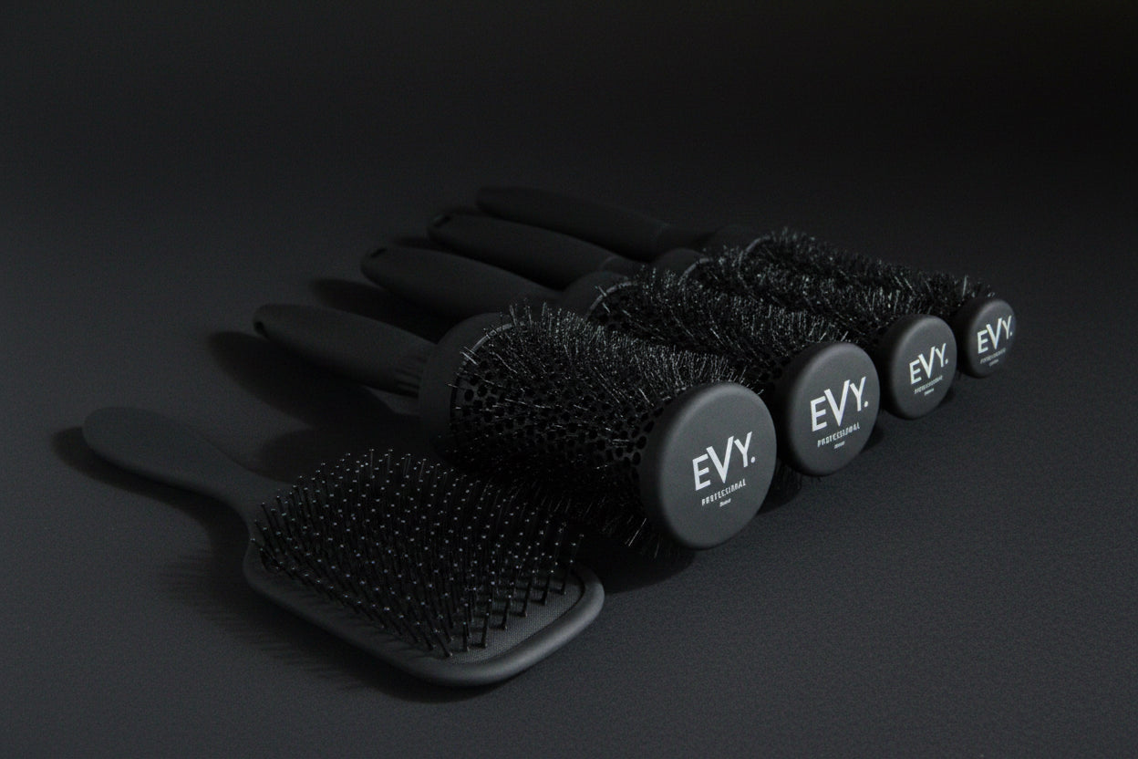 Five black hairbrushes from the brand EVY, including three round brush styles and two paddle brush styles, arranged on a light gray background.